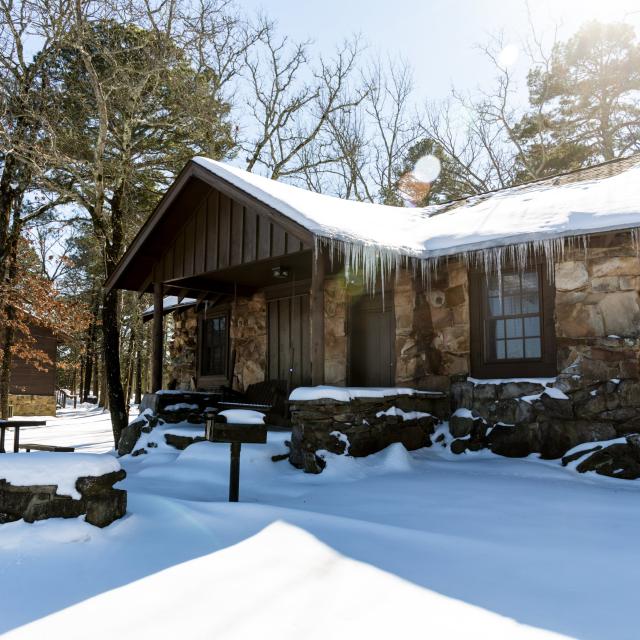 An exterior view of a cabin in winter surrounded by snow at Petit Jean State Park
